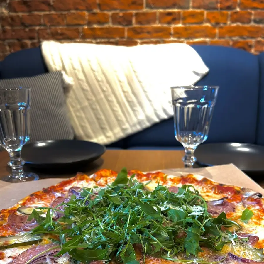 Pizza z rukolą na stole nakrytym do posiłku, obok kieliszki.