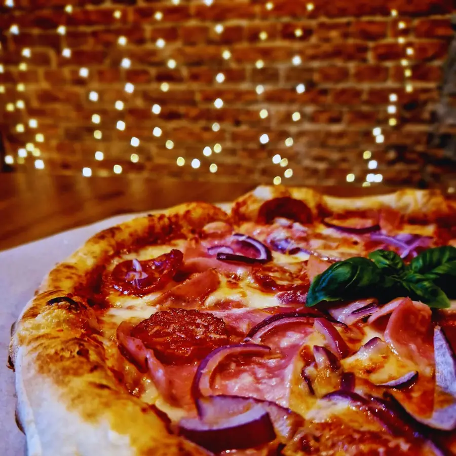 Pizza na blacie, w tle ceglana ściana i lampki.