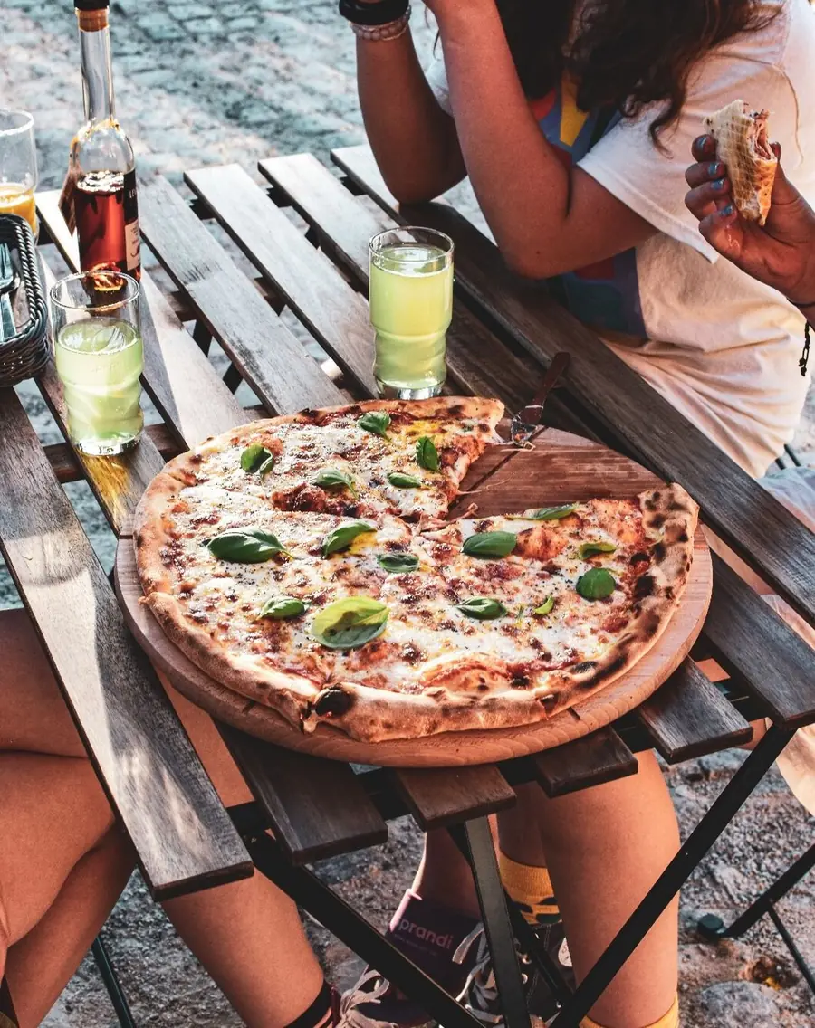 Pizza i napoje na stole w ogródku, w tle nogi siedzących gości.