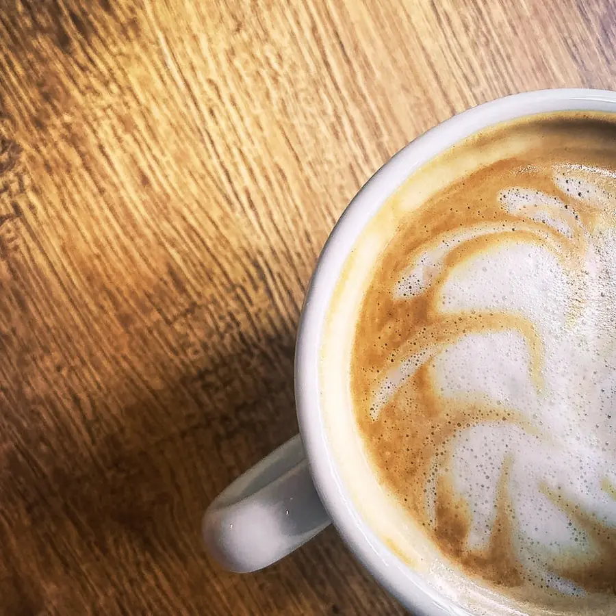 Filiżanka cappuccino z wzorem na piance, trzymana w dłoniach.