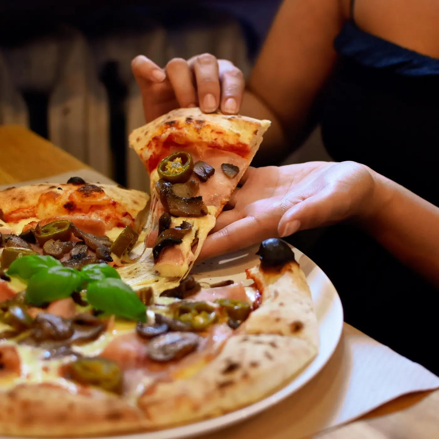 Dłoń unosi kawałek pizzy z jalapeño znad talerza.