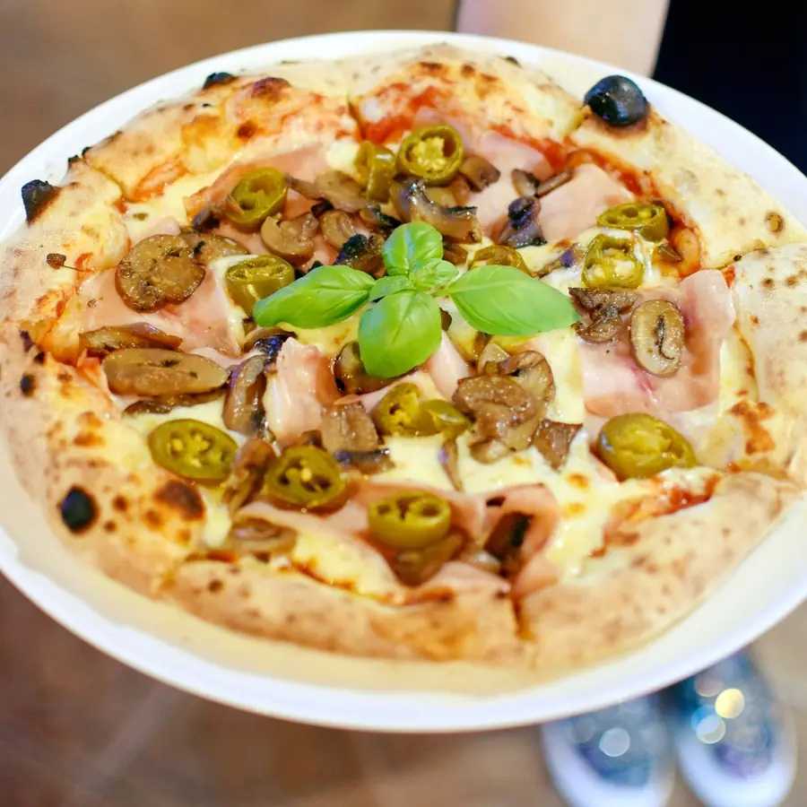 Pizza z jalapeño, oliwkami i bazylią na białym talerzu.