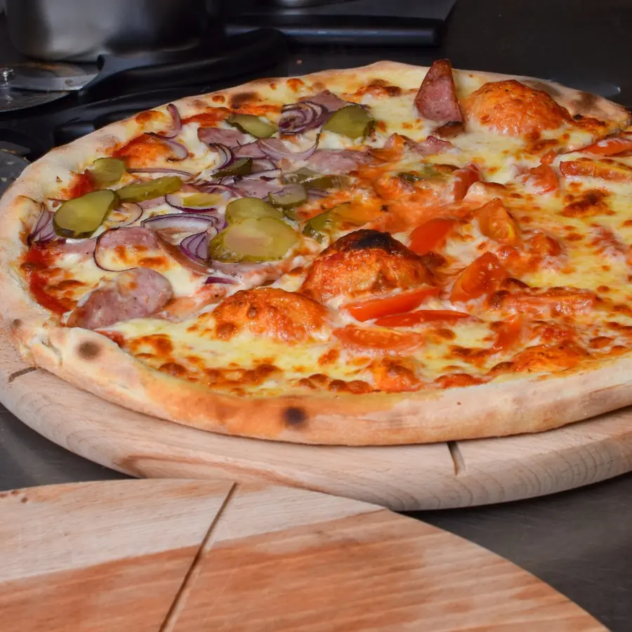 Pizza na okrągłej drewnianej desce, na wierzchu boczek i cebula.
