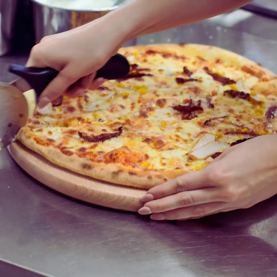 Ręce zsuwają upieczoną pizzę z łopaty na drewnianą deskę.