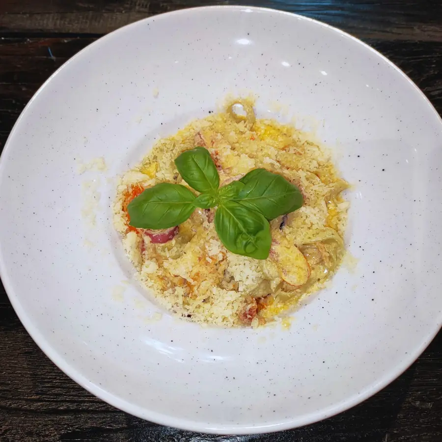 Zielone tagliatelle z kurczakiem na białym talerzu, z listkiem bazylii.